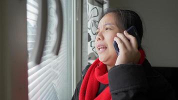 donna asiatica che cammina verso la finestra, apre la tenda e guarda fuori dalla finestra, quindi usa il telefono per chiamare la sua amica, ha una conversazione seria al telefono e vede la vista fuori video