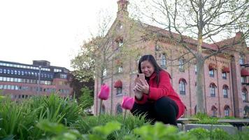 mulher asiática caminhando e sentada para tirar uma foto da bela flor rosa na cidade, passando um tempo maravilhoso, relaxando e vendo a beleza natural. fundo da cidade. sair para passear video