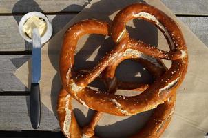 gran pretzel, mantequilla y cuchillo en la mesa de madera en el jardín. foto