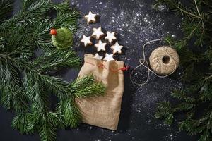 decoración festiva, galletas de canela tradicionales y ramas de árboles de Navidad en la mesa oscura. foto