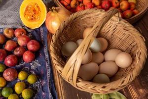 The eggs and other fruits and vegetables in the basket are on the wood grain table photo