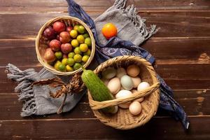 The eggs and other fruits and vegetables in the basket are on the wood grain table photo