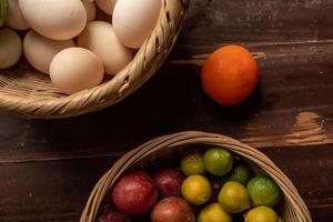 The eggs and other fruits and vegetables in the basket are on the wood grain table photo