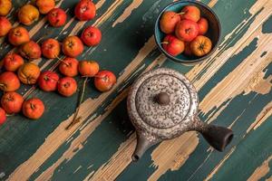 The red hawthorn in the plate and the teapot are on the wooden table photo