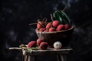 Litchi is placed in a wooden plate, peeled or unopened, on a dark wood grain table photo