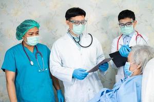 El equipo médico asiático revisa a la anciana paciente en busca de enfermedad para motivarla nueva normalidad para tratar la infección Covid-19 coronavirus en la sala del hospital foto