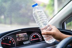 Conductor de mujer asiática sosteniendo una botella para beber agua mientras conduce un automóvil. la botella de agua caliente de plástico causa un incendio foto