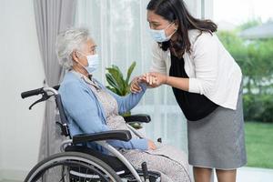Ayude a una anciana asiática mayor o anciana sentada en una silla de ruedas y con una mascarilla para proteger la seguridad de la infección por el coronavirus covid-19 foto