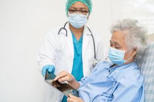 Doctor help Asian senior or elderly old lady woman patient wearing a face mask in hospital for protect safety infection and kill Covid-19 Coronavirus photo