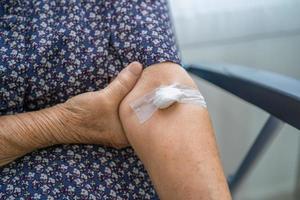 Asian senior or elderly old lady woman patient show cotton wool stop bleeding, after blood drawing testing for annually physical health check up to check cholesterol, blood pressure, and sugar level photo