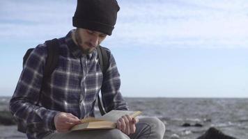 ung manlig resenär med bok på stranden med ryggsäck video
