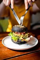 Hands cut Broccoli quinoa charcoal burger with guacamole by knife.