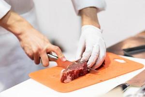 Chef cutting fresh raw meat with knife in the kitchen photo
