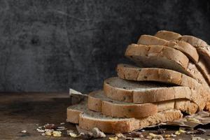 Pan de trigo integral de grano en rodajas sobre fondo de madera rústica oscura foto