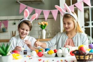 dos niños felices con orejas de conejo pintan huevos de Pascua en la mesa. foto