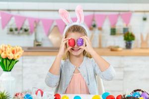 niña sonriente cierra los ojos con huevos de pascua en la cocina. foto