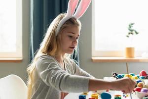 Smiling blond girl paints Easter eggs. Side view. photo