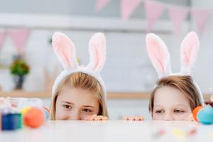 dos niños miran desde debajo de la mesa, miran los huevos de pascua. diviértete en la cocina. foto