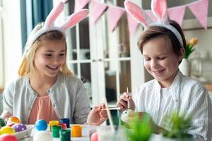 dos niños alegres pintan huevos de pascua en orejas de conejo. foto