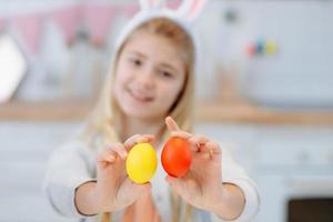 Young, cute girl in bunny earsshowing a hand-made eggs. Easter traditions. photo