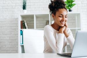 sonriente, atractiva chica trabajando en la computadora, sentada en la mesa foto