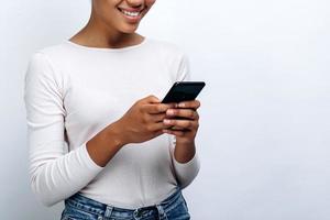 Linda chica sonriente con un teléfono en sus manos sobre un fondo de una pared blanca, vista cercana foto