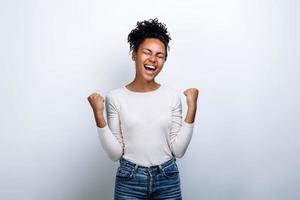 Victorious gesture. The girl on a background of a white wall rejoices in the victory photo