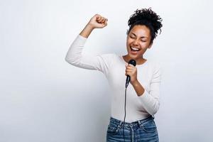 linda chica canta en un micrófono, se divierte cantando sobre un fondo blanco foto