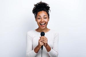 Chica alegre con un micrófono en sus manos sobre un fondo de pared blanca foto