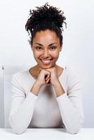 Retrato de estudio de una hermosa chica morena sobre un fondo blanco sentada en la mesa foto