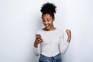 Young girl make a gesture of a winner holding a phone in his hand on a white background photo