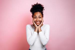 Linda chica afro se regocija sinceramente en un fondo de pared rosa foto