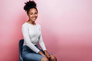 Adorable, beautiful girl sitting on a chair isolated on a background of a pink wall photo