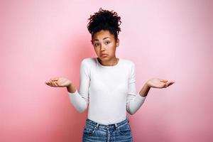 Closeup of emotional young woman isolated on pink background being at a loss, showing helpless gesture with arm and hands photo