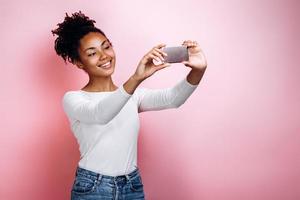 Retrato de niña bonita realizando selfie apagado sobre fondo de color rosa foto