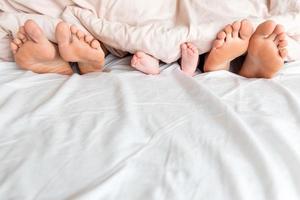 las piernas de un niño, mamá y papá se asoman debajo de la manta blanca foto