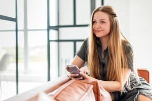 hermosa niña sentada en el sofá sosteniendo un teléfono en sus manos, mirando a otro lado foto