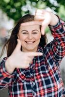 Portrait of playful beautiful caucasian woman pretending to take photo with her hands while walking on the street. Attractive model posing, using hands to make a frame outdoors