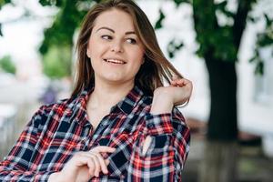 Cute girl in a checkered shirt straightens her hair outdoors photo