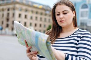 hermosa joven turista se encuentra en la plaza, estudiando cuidadosamente el mapa turístico foto