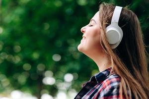 Perfil facial de una mujer bonita y relajada en auriculares sobre un fondo de naturaleza, foto