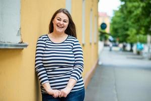 Smiling beautiful woman plus size looking straight into the camera on the street over orange background photo