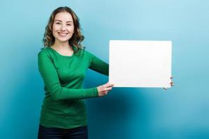 Smiling girl demonstrates white blank space for text on the side. Closeup, on blue background. photo