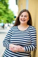 A beautiful, sweet, smiling lady leaned against an orange wall outdoors photo