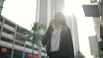 Asian businesswoman walking in the street while using a smartphone and holding a coffee cup video