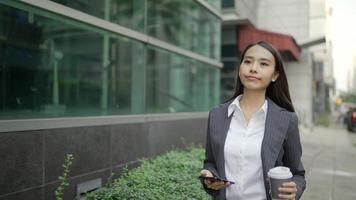 Asian businesswoman walking in the street while using a smartphone and holding a coffee cup video