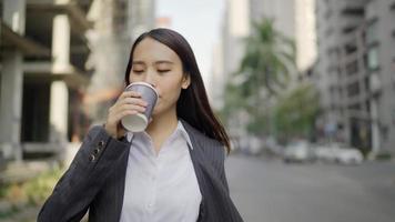 Asiatische Geschäftsfrau, die auf die Straße geht, während sie ein Smartphone benutzt und eine Kaffeetasse hält video
