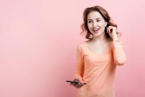 Cheerful girl in AirPods with phone dancing, pink background. photo