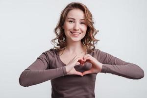 Smiling young girl making heart with fingers. On a white background.
