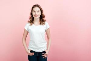 Mujer joven y hermosa en camiseta blanca y jeans posando sobre fondo de pared rosa